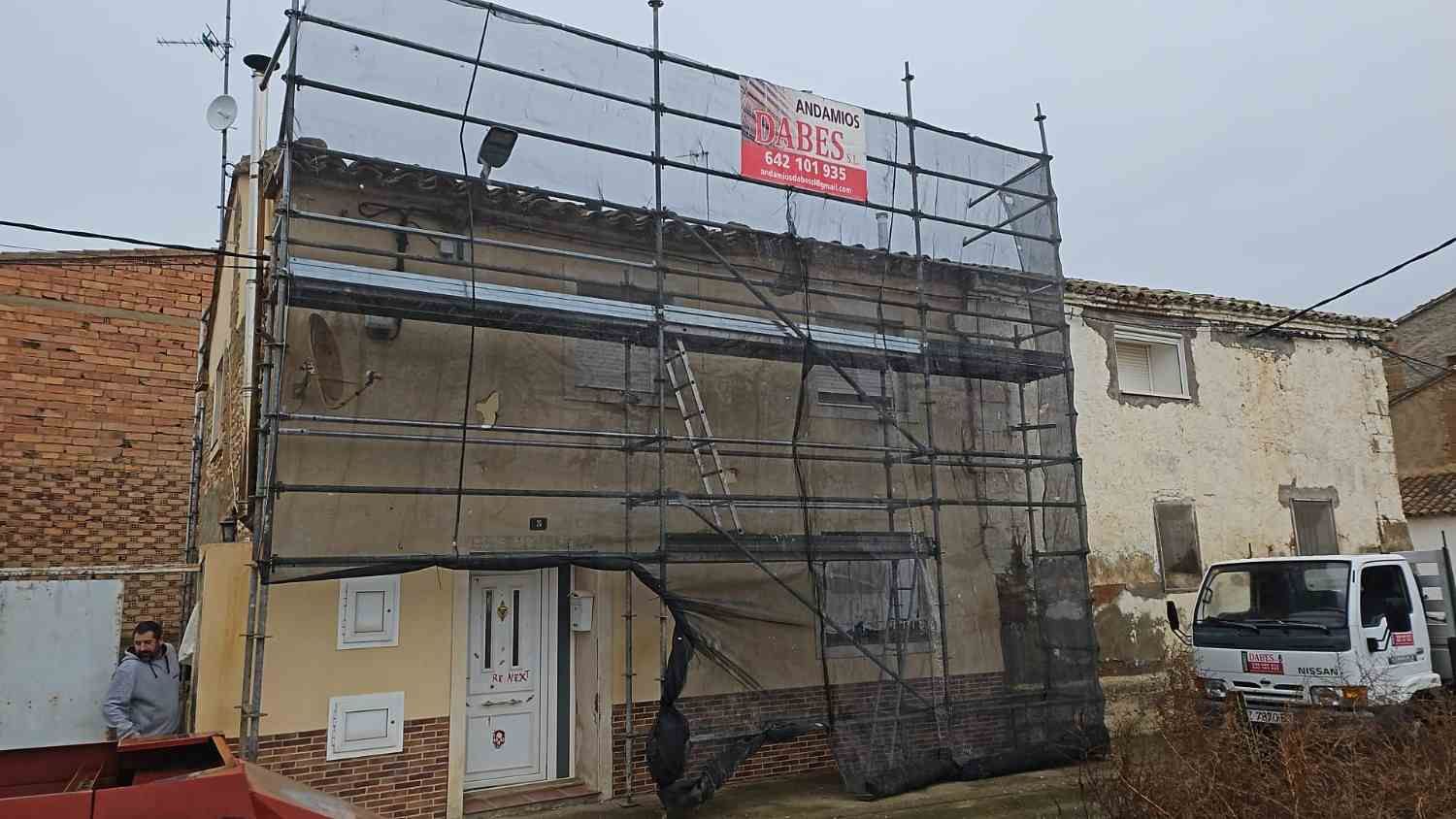 Edificio en obras de renovación, con andamios y mallas, junto a una furgoneta blanca en una calle
