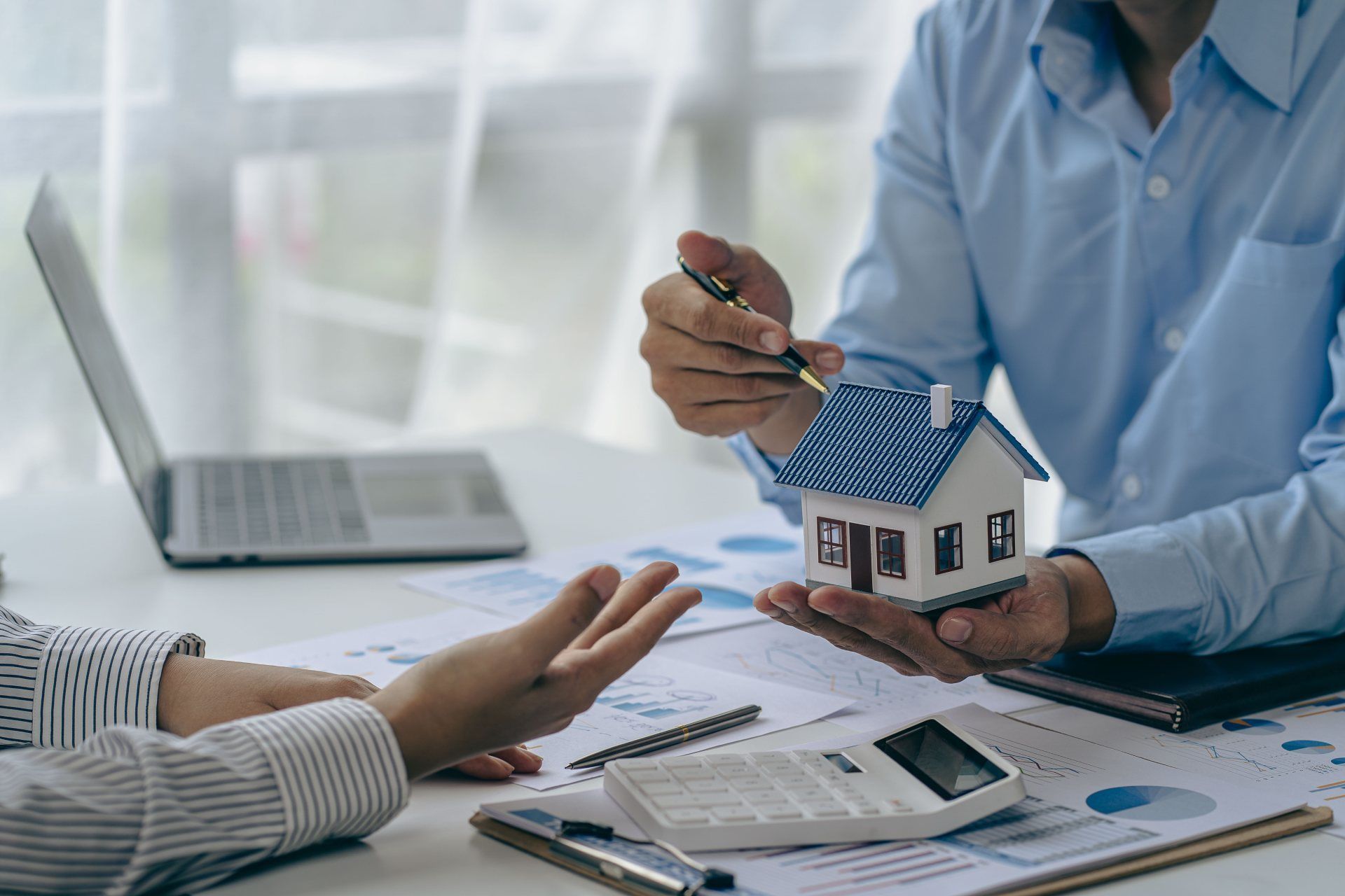 Ein Immobilienberater sitzt an einem Tisch und hält ein Modellhaus in seinen Händen.