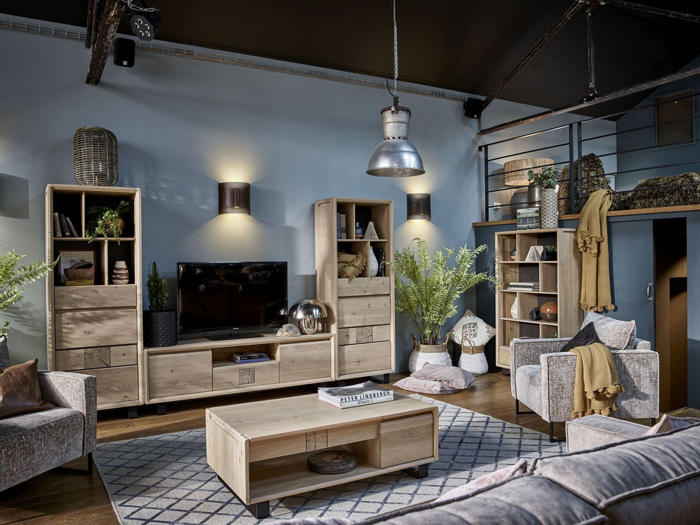 Salon avec meubles en bois clair, murs bleus et éclairage industriel.