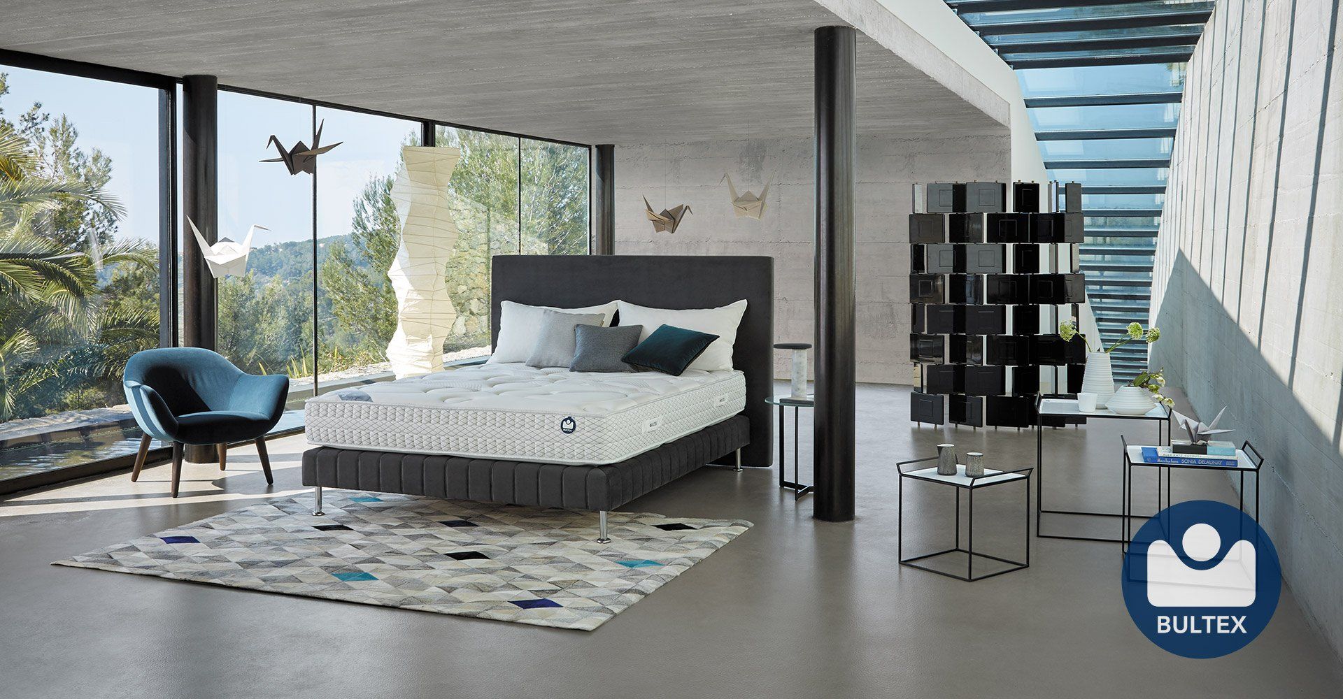 Chambre moderne avec lit, fauteuil, grandes fenêtres et tapis.