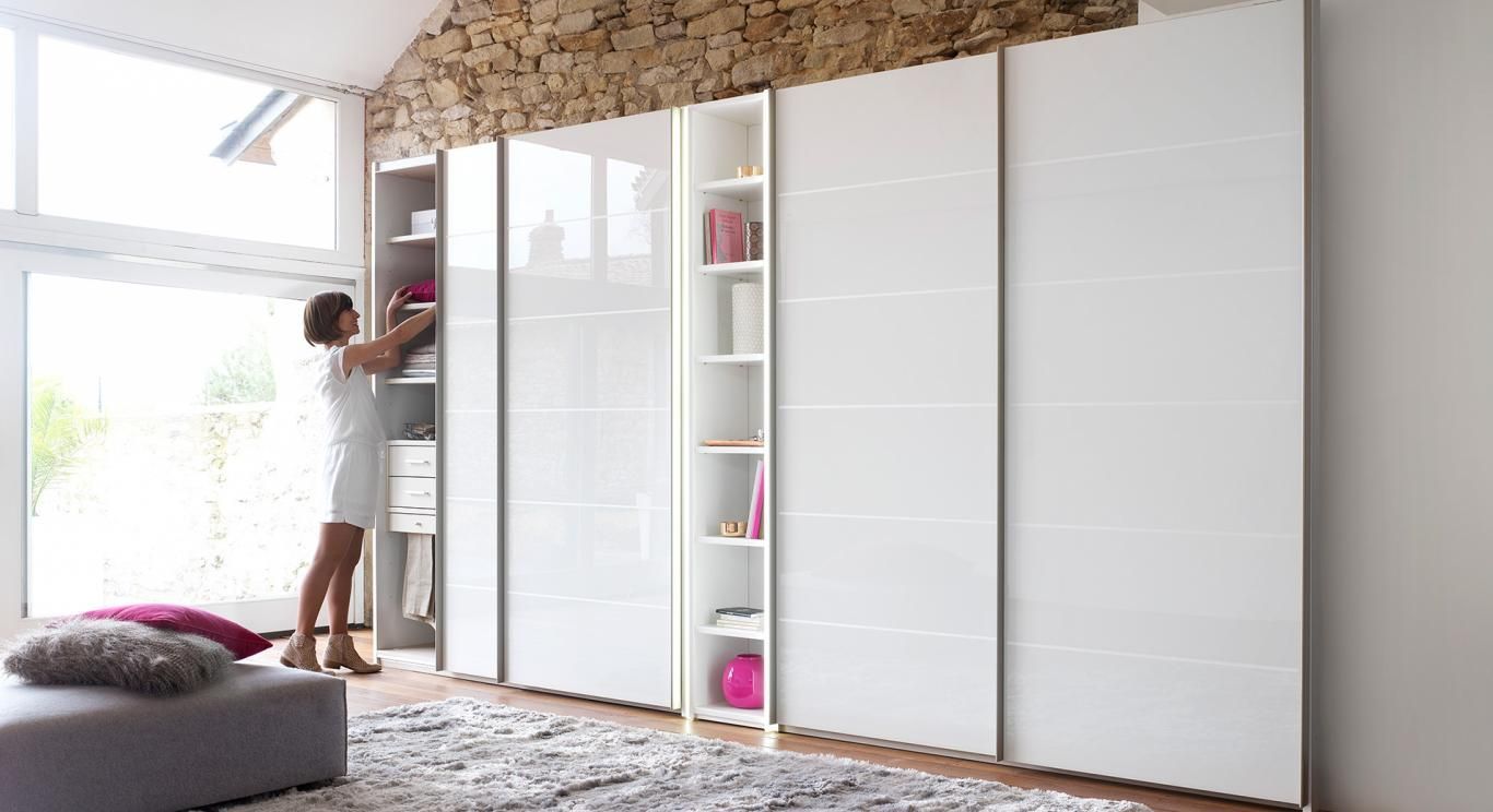 Femme rangeant des affaires dans un placard blanc à portes coulissantes. Intérieur lumineux, étagères, couleurs neutres.