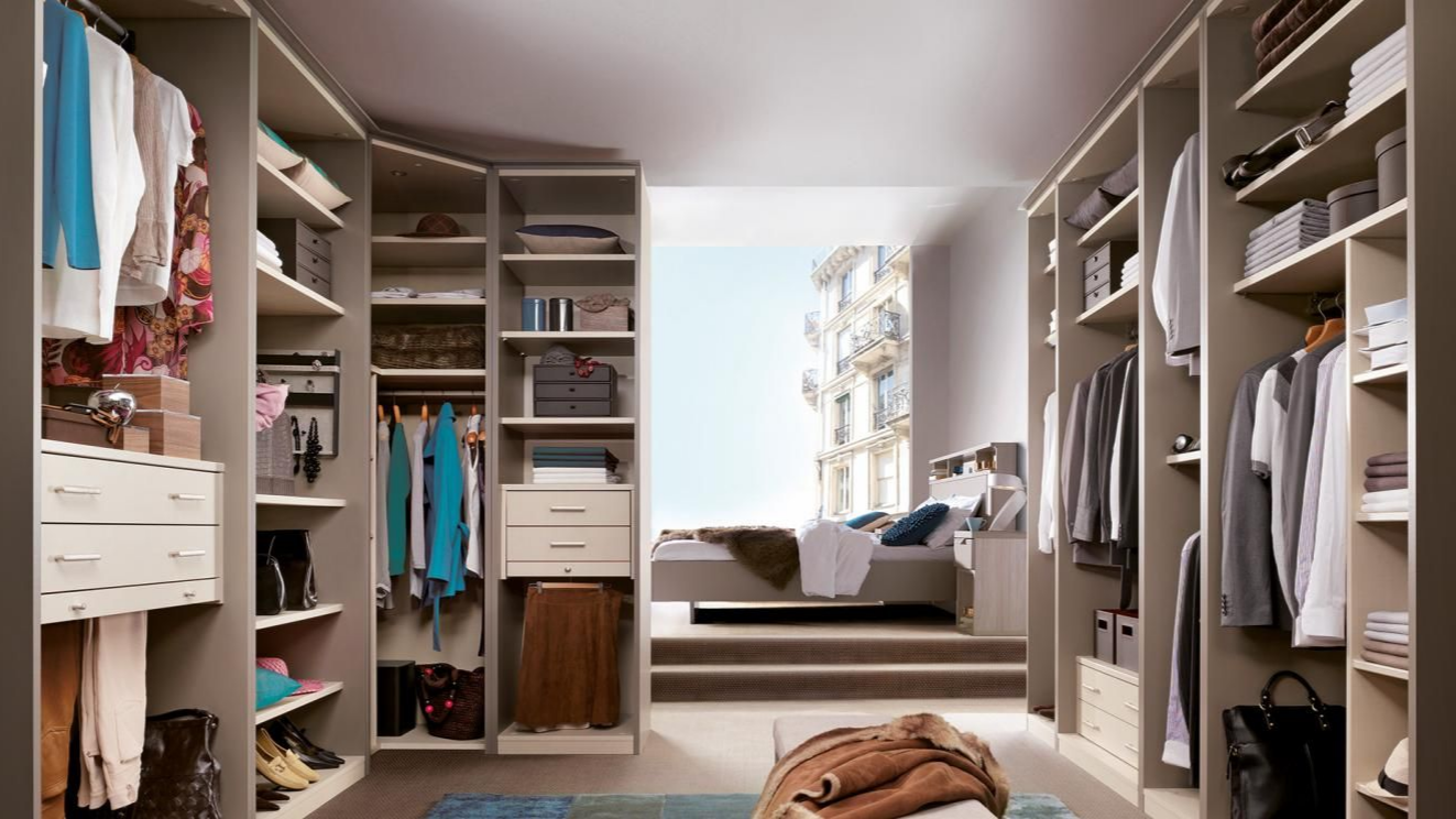 Dressing avec étagères beiges, vêtements et un lit en arrière-plan avec vue.