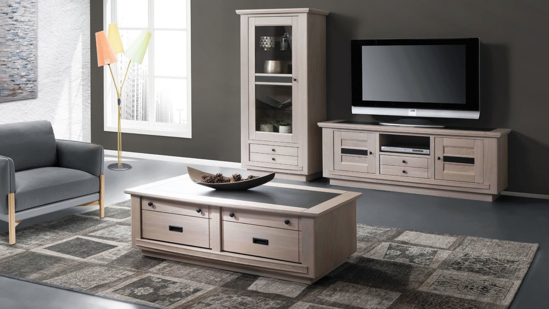 Salon avec meubles en bois clair, comprenant un meuble TV, une vitrine, une table basse et un fauteuil sur un tapis à motifs.