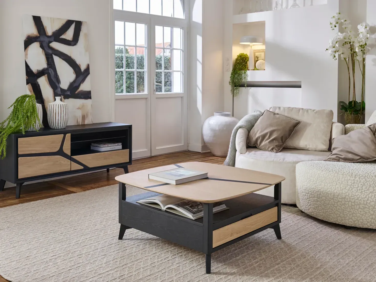 Salon avec table basse relevable et meuble TV. Canapé beige, tapis neutre et œuvres d'art abstraites.