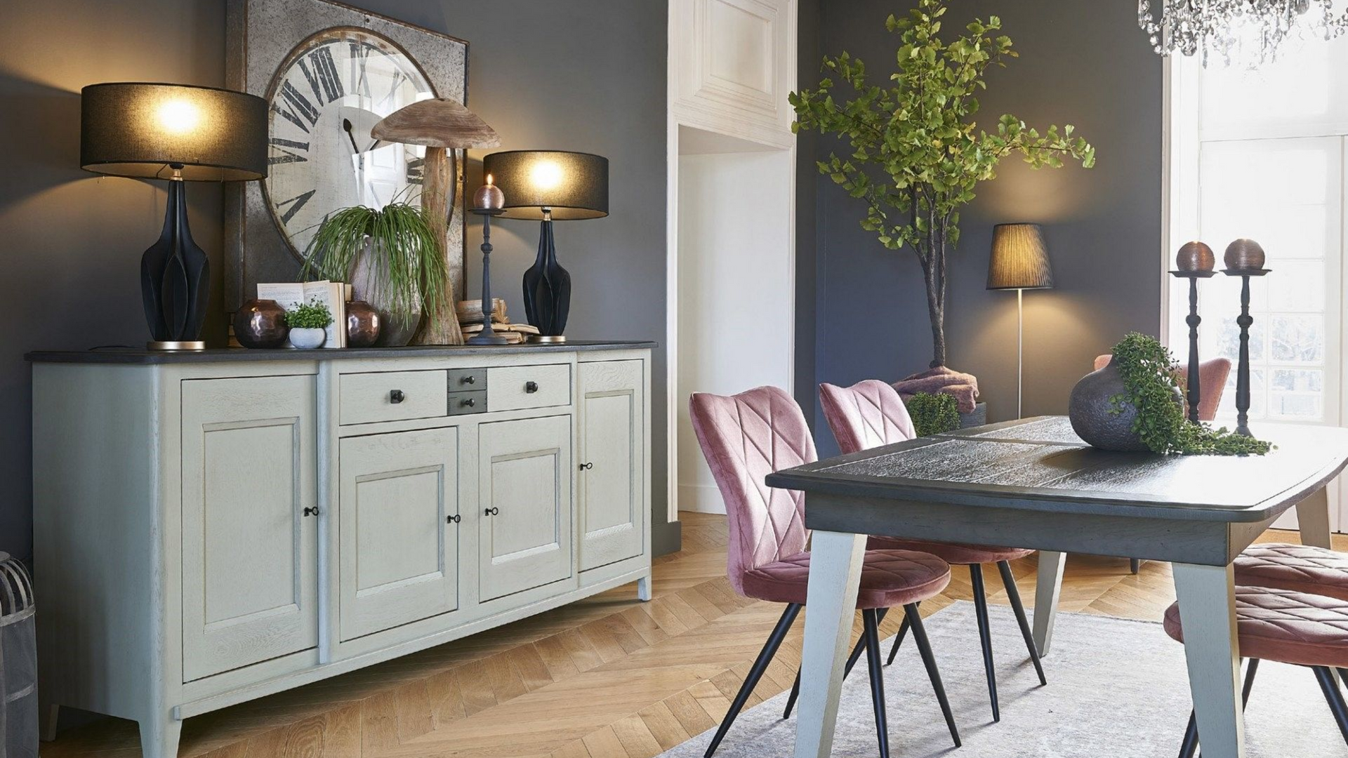 Salle à manger avec buffet gris, table, chaises en velours et décoration.