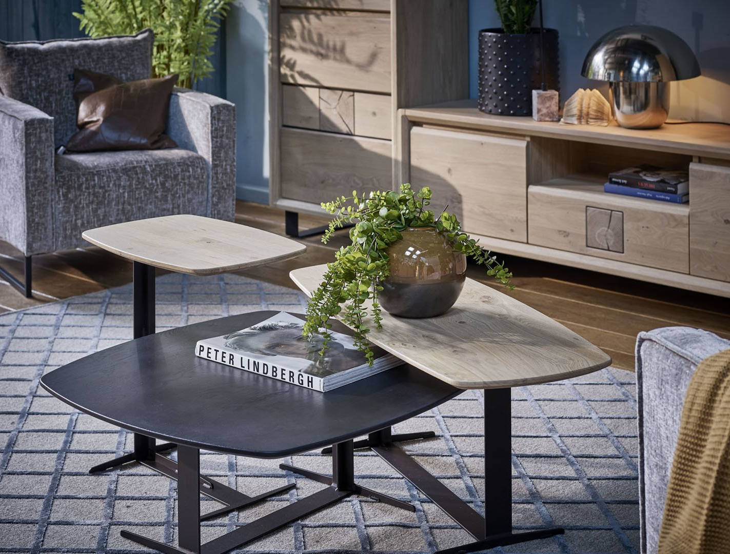 Salon avec tables basses à trois niveaux, fauteuil gris, armoire en bois et plantes décoratives.