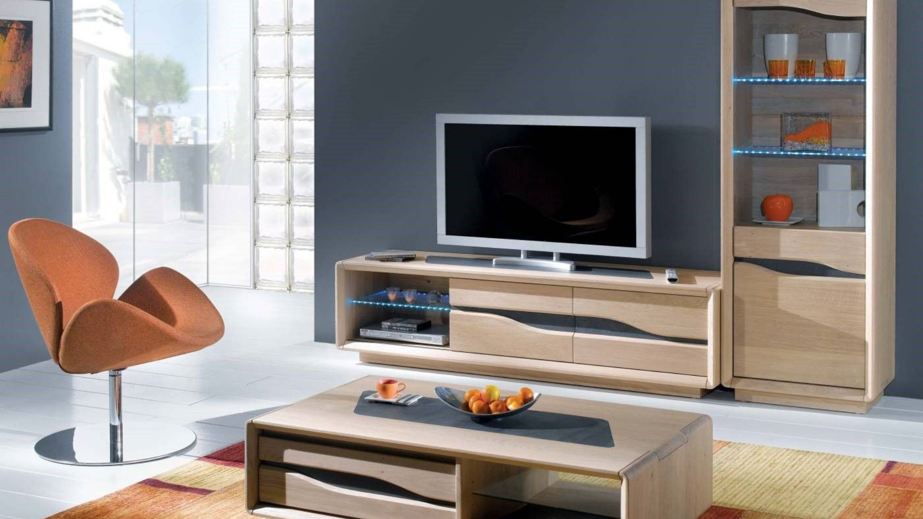 Salon avec meubles en bois, télévision moderne, fauteuil orange et mur gris.