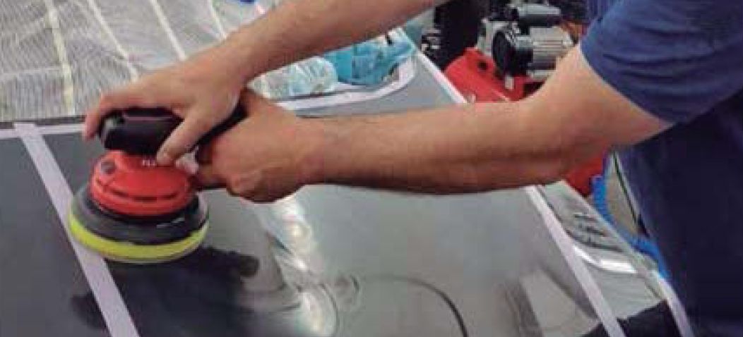 Una persona utiliza una pulidora orbital de doble acción, de color rojo y amarillo, para pulir el capó de un coche.