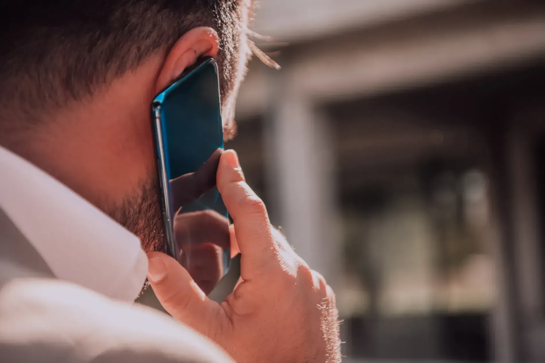 Hombre sosteniendo un teléfono inteligente azul en su oreja, al aire libre.
