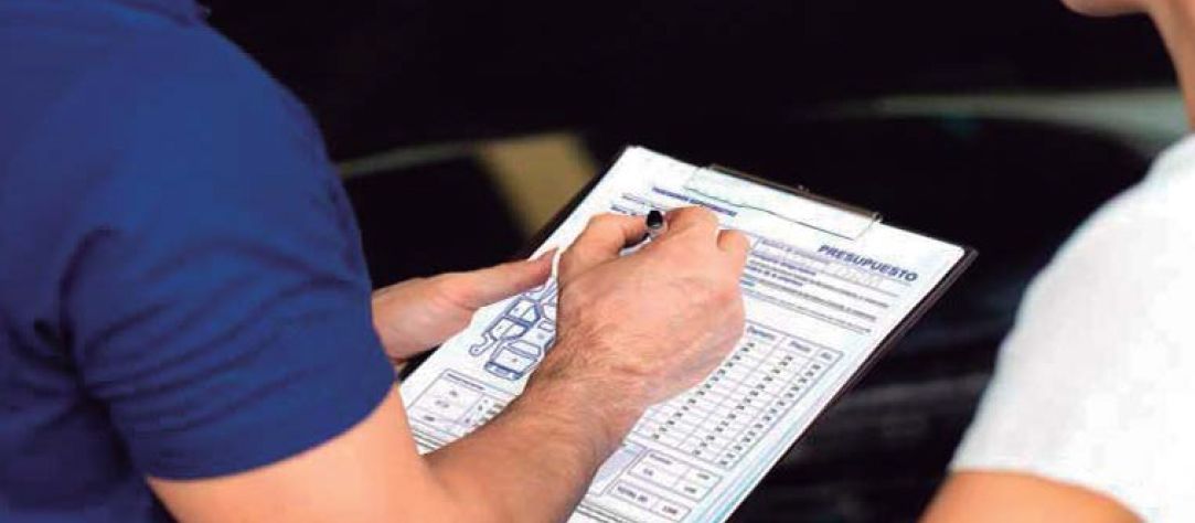 Una persona con camisa azul escribiendo en un portapapeles durante una consulta.
