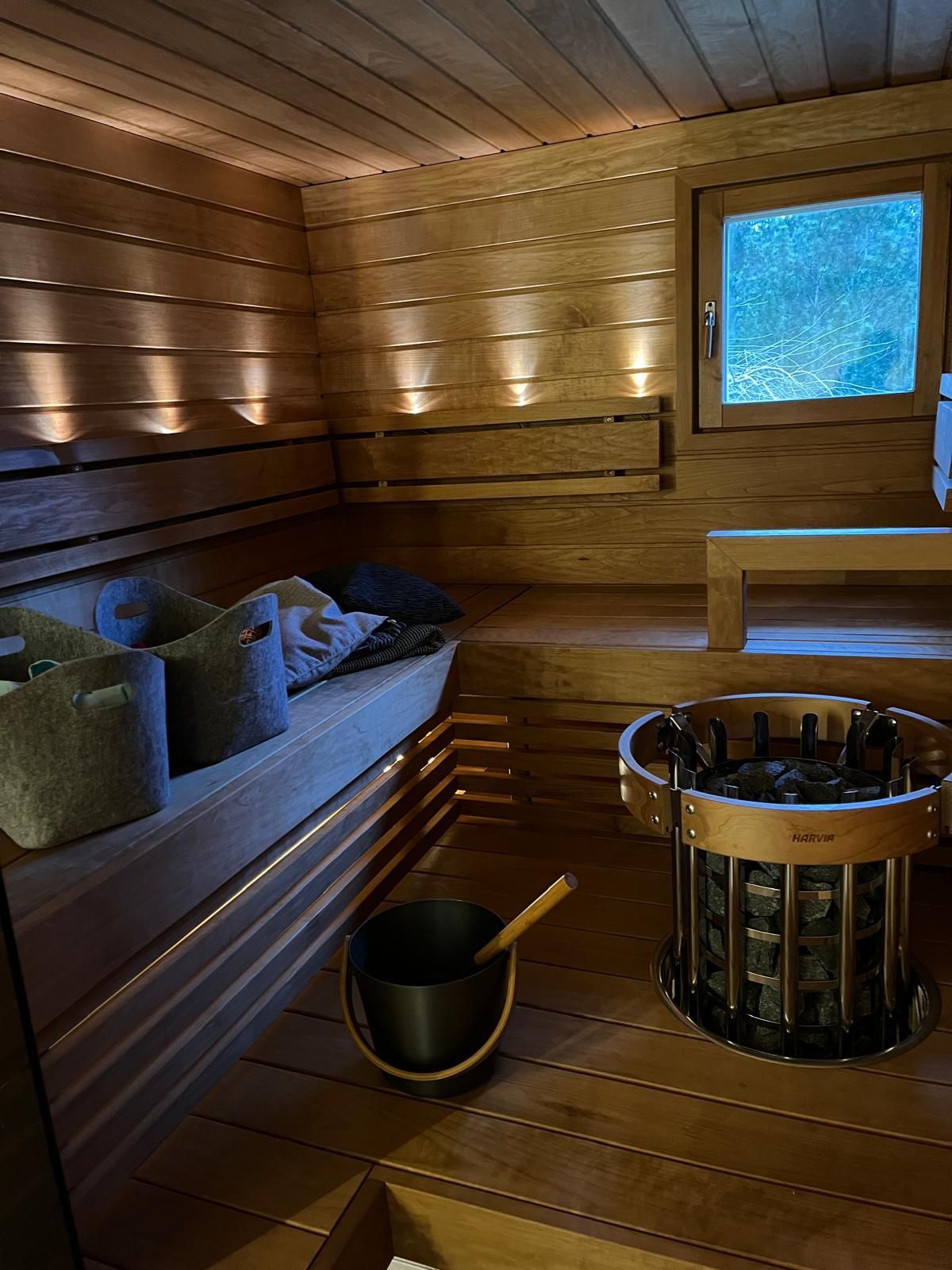 Tunnelmallinen musta saunasisustus, jossa on lauteisiin upotettu kiuas ja tummat paneelit Liedon kohteessa.
