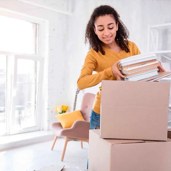 Una mujer sostiene una pila de libros en una caja de cartón.