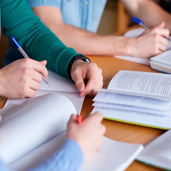 Un grupo de personas está sentado en una mesa con libros y bolígrafos en sus manos.