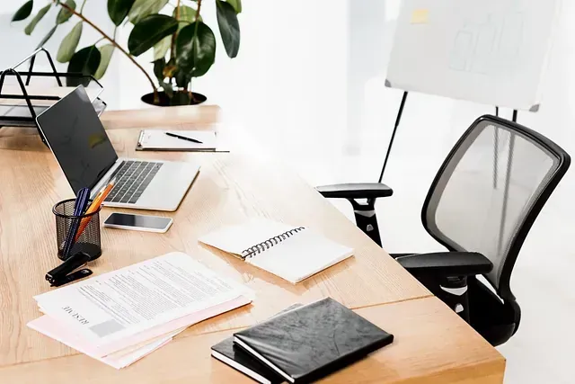 Un escritorio con una computadora portátil, cuadernos, papeles y una silla.