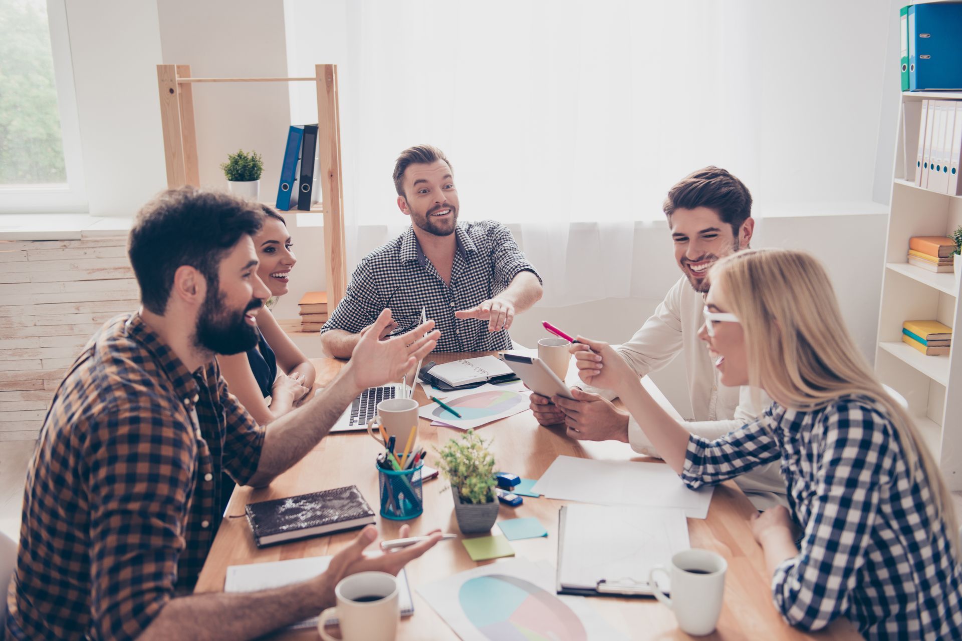 Un grupo de personas colabora alrededor de una mesa en una oficina. Gesticulan, sonríen y debaten ideas.