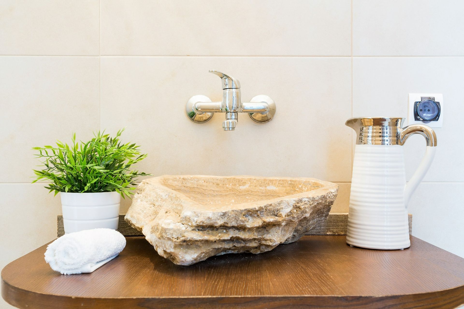 Un baño con un lavabo de piedra y una jarra sobre una encimera de madera.