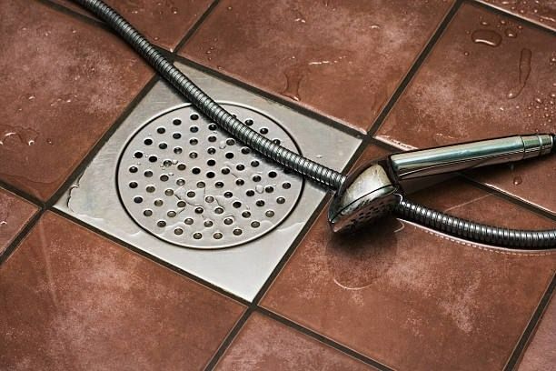 Un cabezal de ducha está colocado sobre un suelo de baldosas al lado de un desagüe.