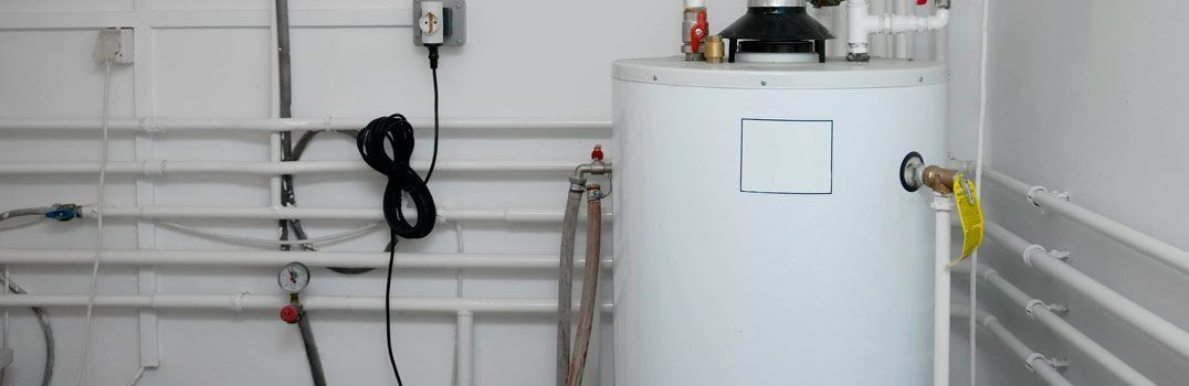 Un calentador de agua blanco está sentado en una habitación al lado de las tuberías.
