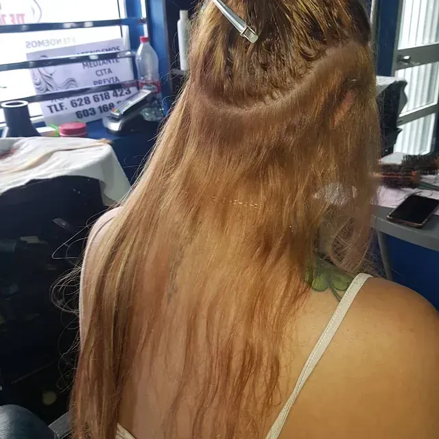 Una mujer con cabello largo y rubio lleva una camiseta blanca sin mangas.