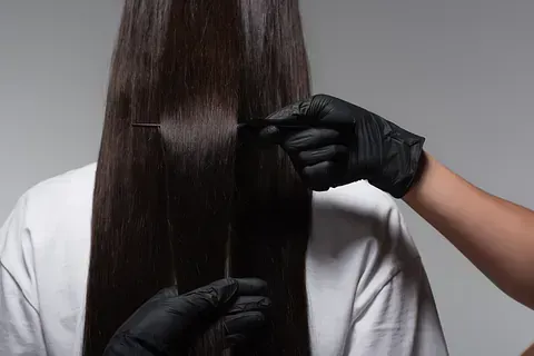 Una mujer se deja alisar el cabello por un peluquero que lleva guantes negros.