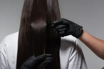 Una mujer se deja alisar el cabello por un peluquero que lleva guantes negros.