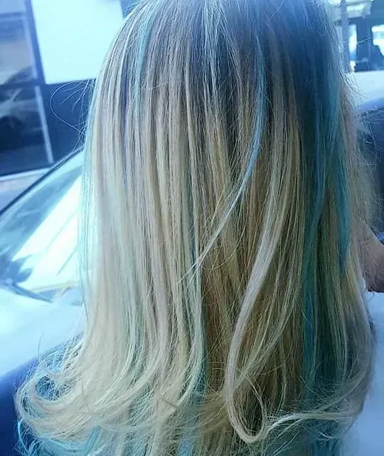 Una mujer con cabello rubio y azul está sentada en un auto.