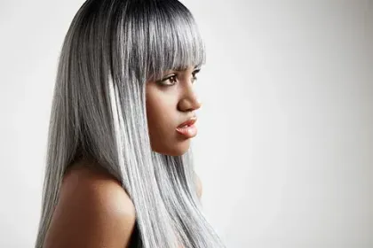 Una mujer con cabello largo y gris y flequillo mira hacia un lado.