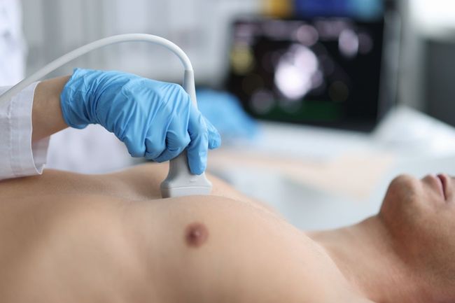 Ein Arzt mit blauen Handschuhen führt eine Ultraschallsonde auf dem Brustkorb des Patienten durch.