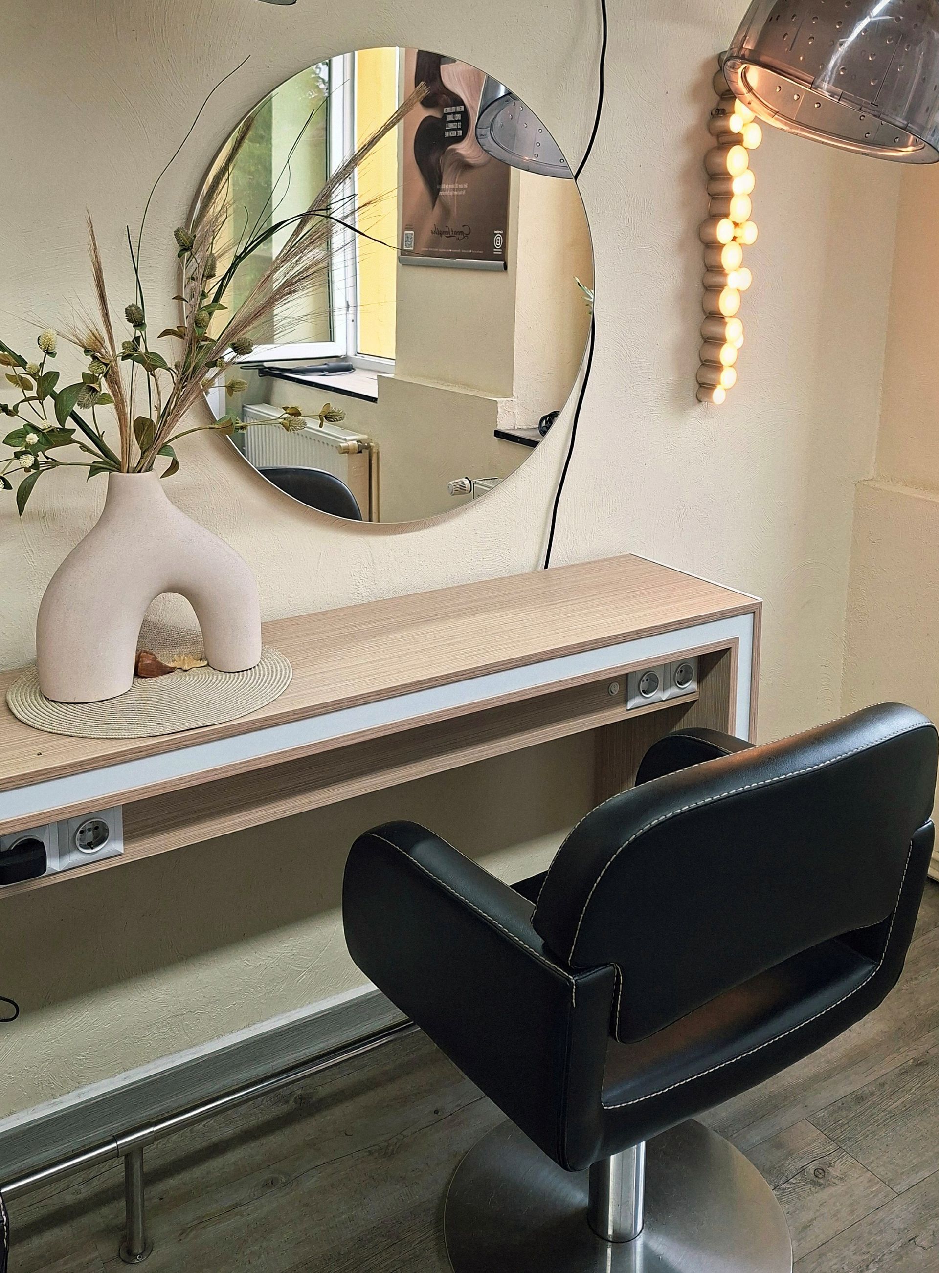 Moderner Salonplatz mit rundem Spiegel, cremefarbener Einrichtung und schwarzem Friseurstuhl