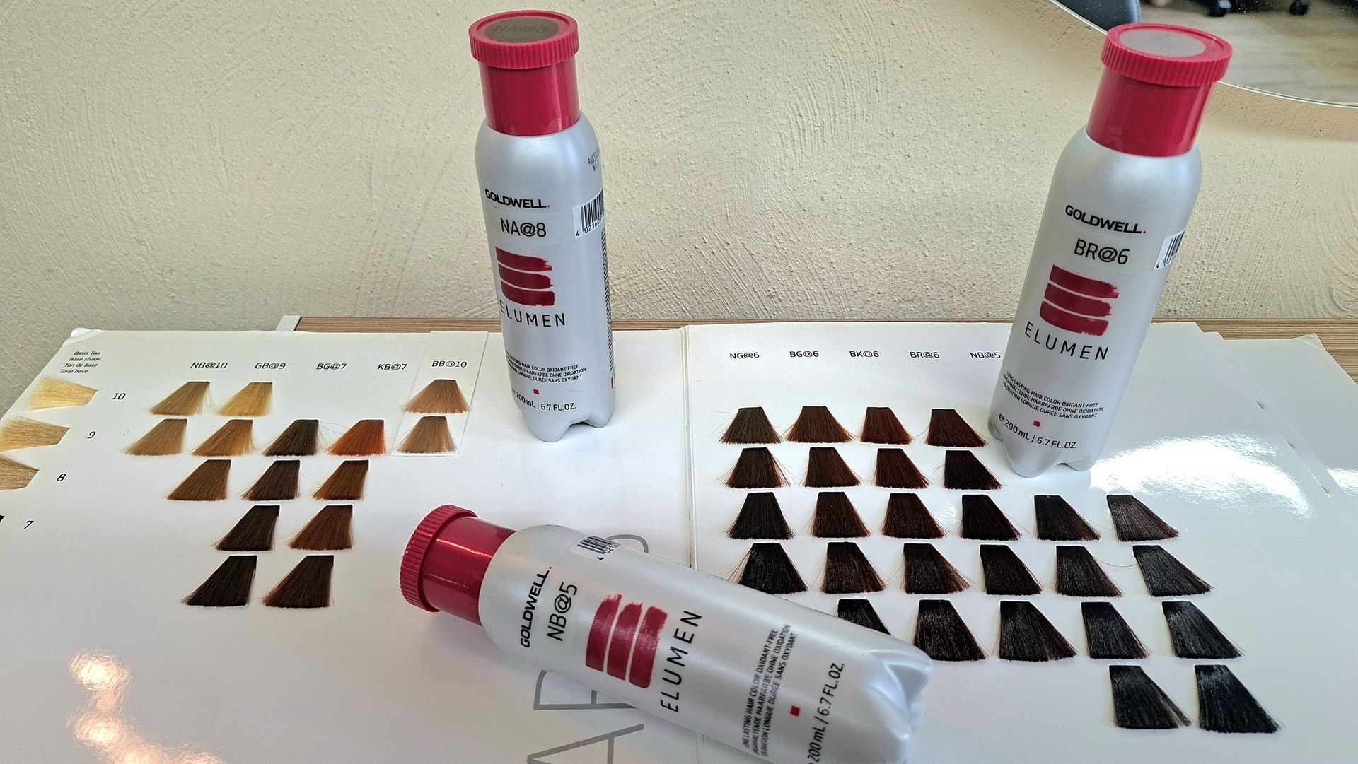 Drei Tuben mit braunem Pigment und schwarze Farbproben auf weißen Tafeln.