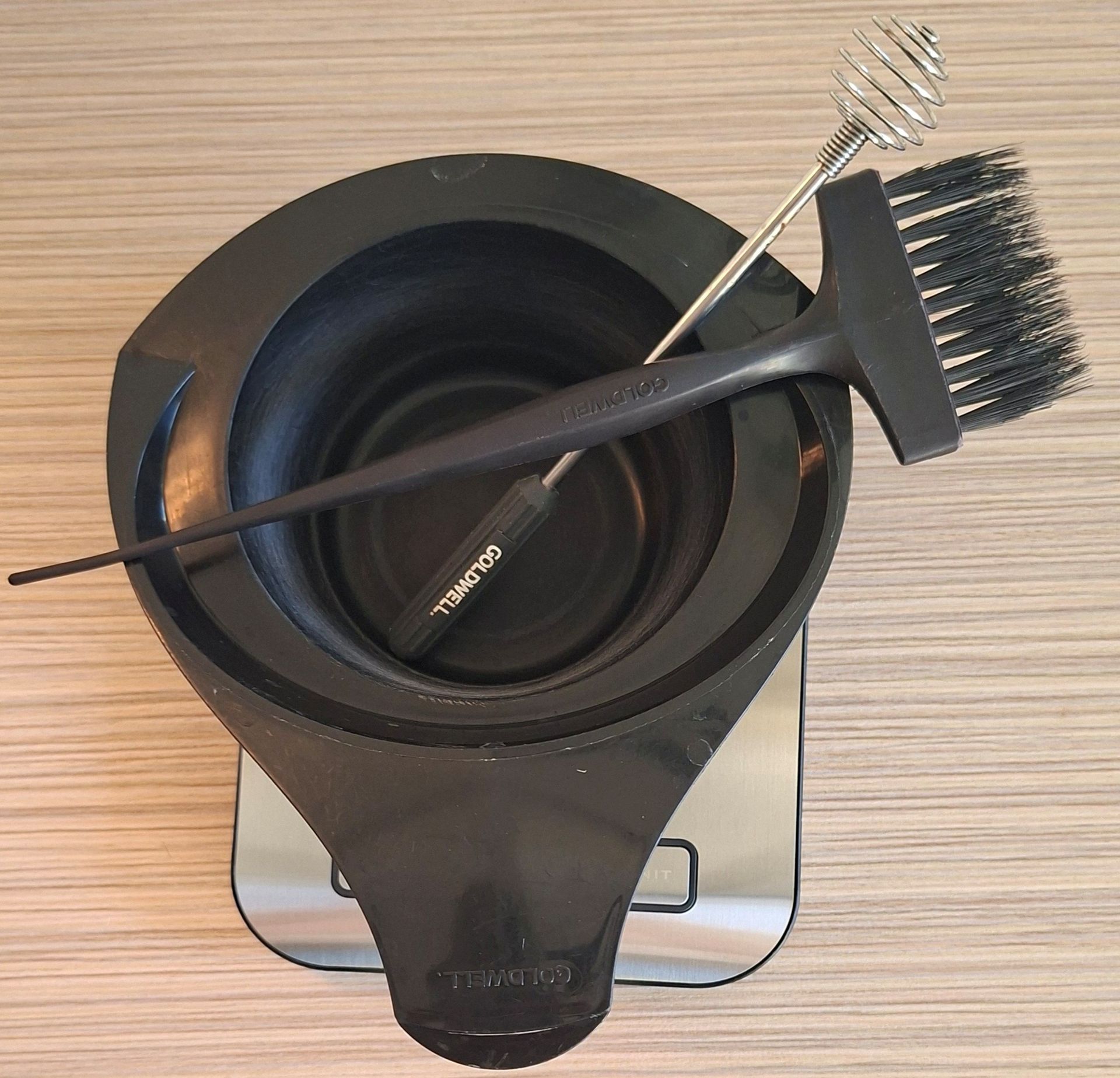 Schwarze Schale mit Haarfärbepinsel, Kamm und Mischutensilien auf einer Holzoberfläche