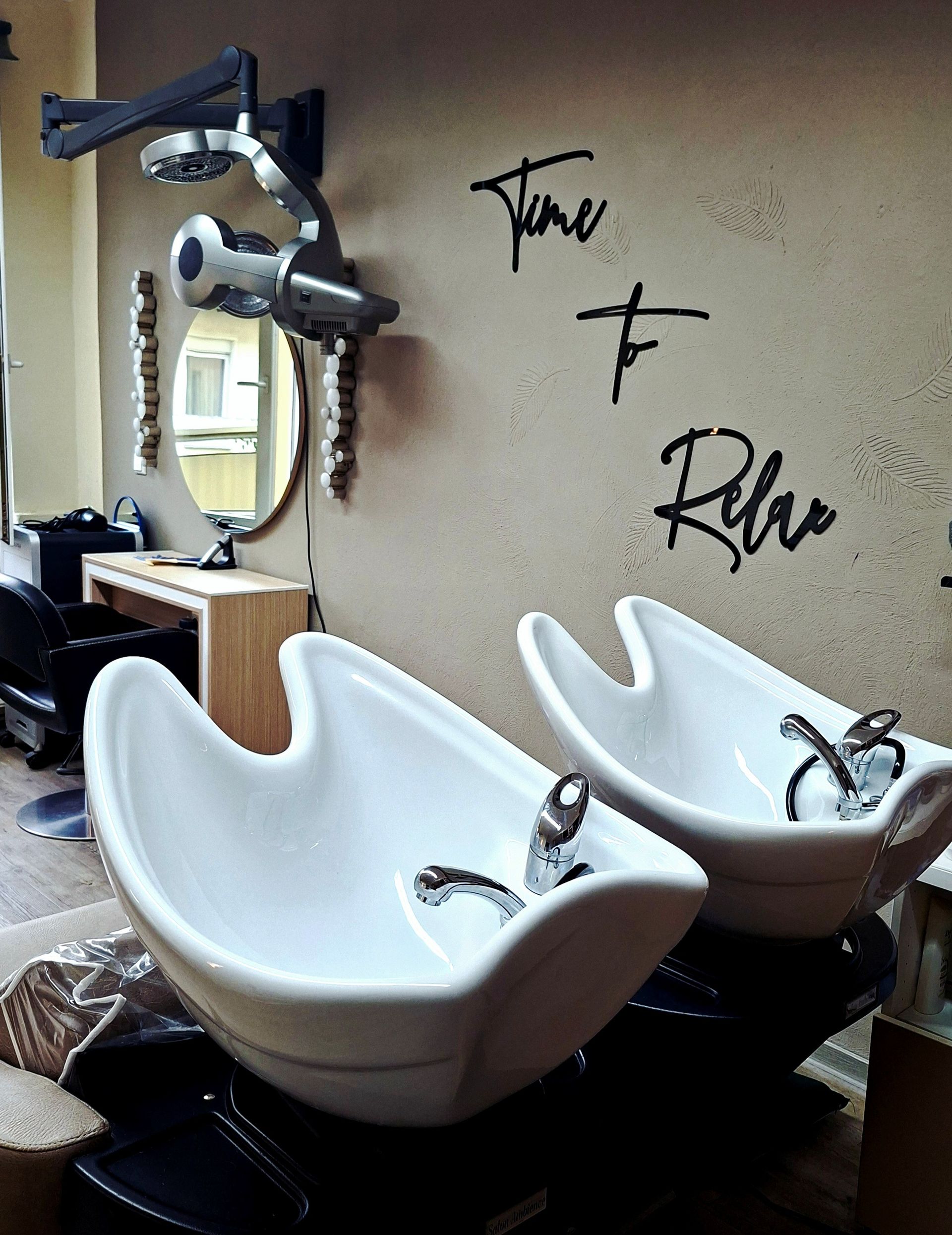 Friseursalon mit zwei weißen Waschbecken und Spiegeln an einer beigefarbenen Wand mit dem Wandtattoo 