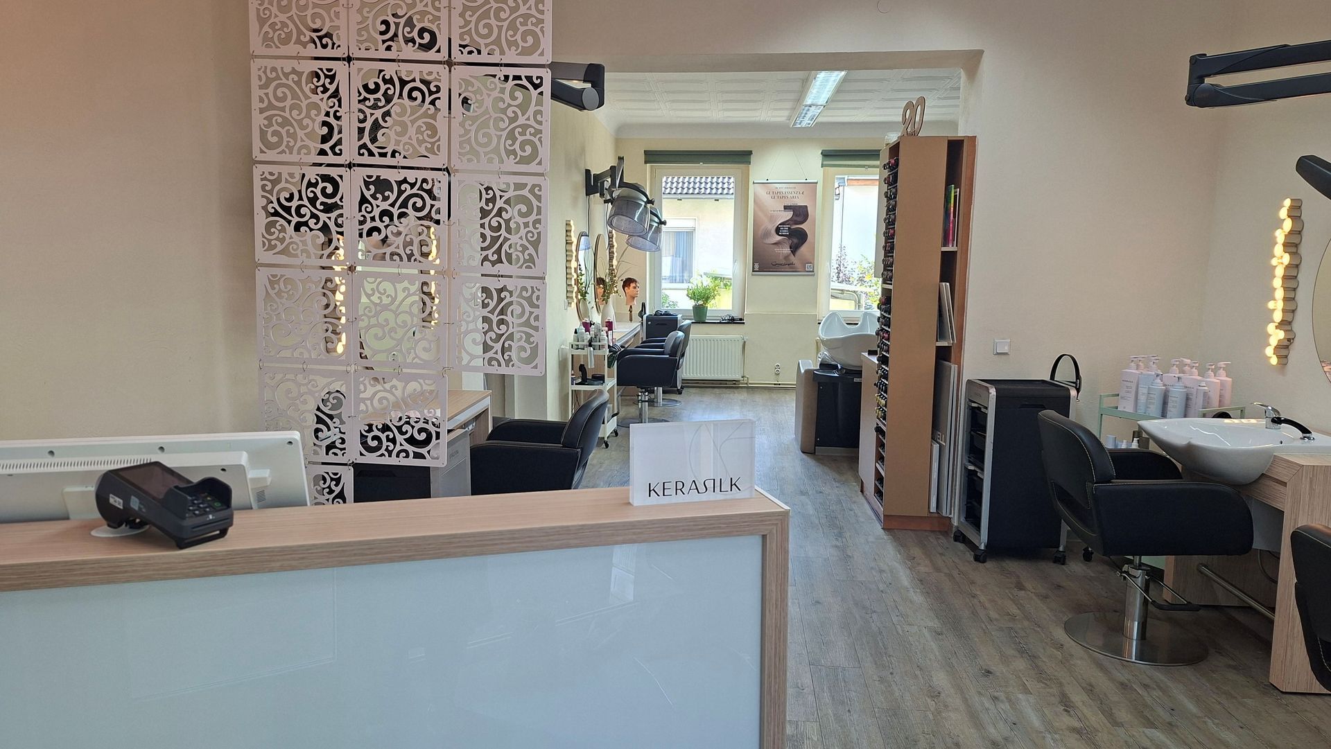 Modernes Saloninterieur mit Empfangstresen, gemustertem Raumteiler, Spiegeln und Stylingplätzen.