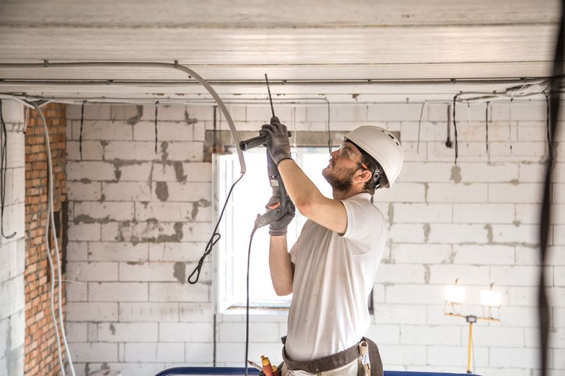 Obrero de la construcción perforando el techo de un edificio en construcción, usando casco y gafas de seguridad.