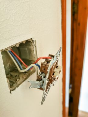 Cableado eléctrico expuesto y placa de interruptor con cables de colores en una pared.