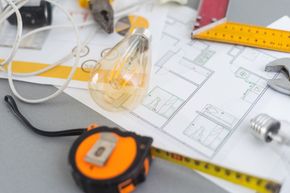 Planos arquitectónicos con herramientas como una bombilla, una cinta métrica y una llave inglesa, que sugieren una renovación del hogar.