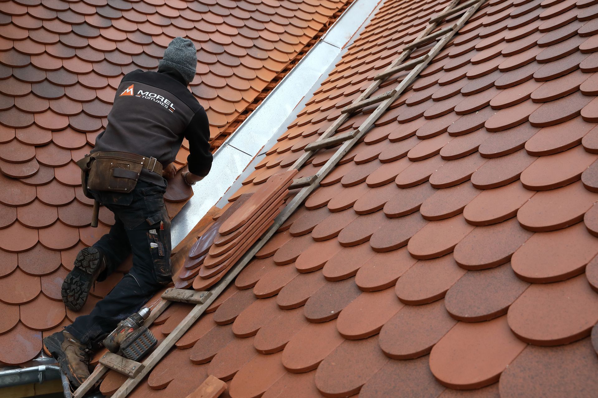 Ouvriers de l'entreprise Morel en train de mettre des tuiles le long d'un chéneau