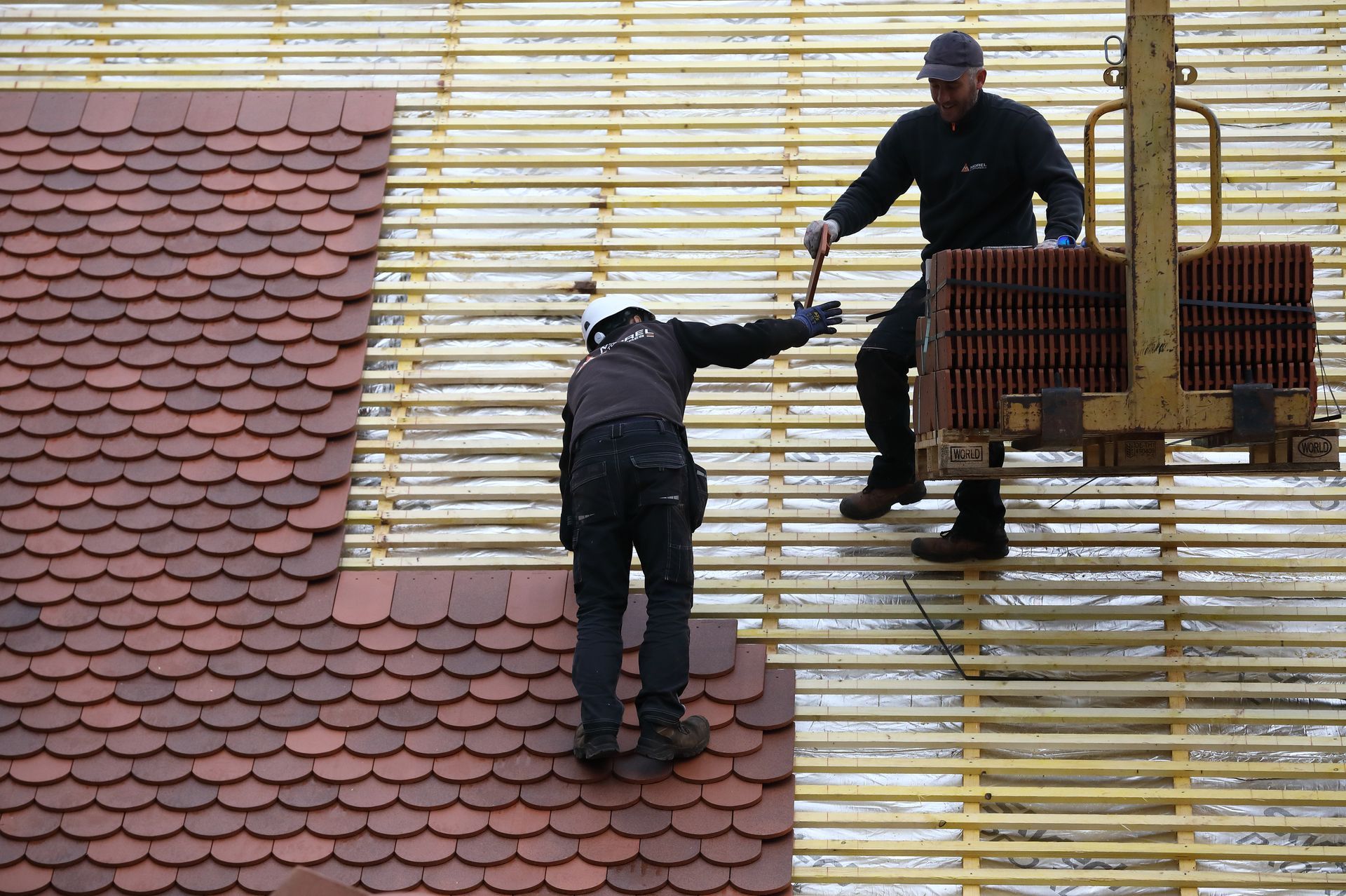 Deux hommes de chez Toitures MOREL posant des tuiles sur un toit