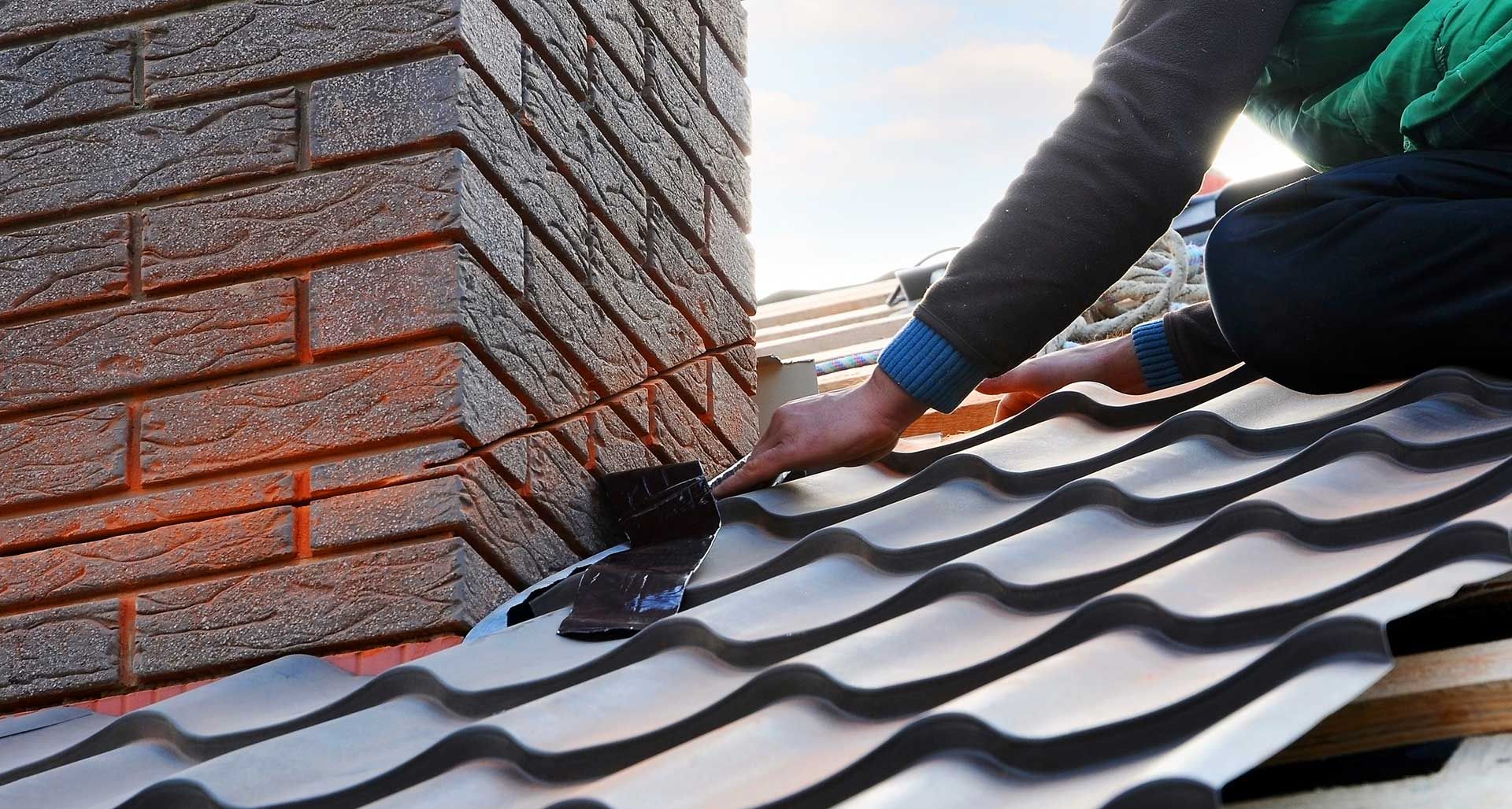 Gros plan sur un homme qui pose une membrane pour l'étanchéité d'une toiture à côté d'une cheminée