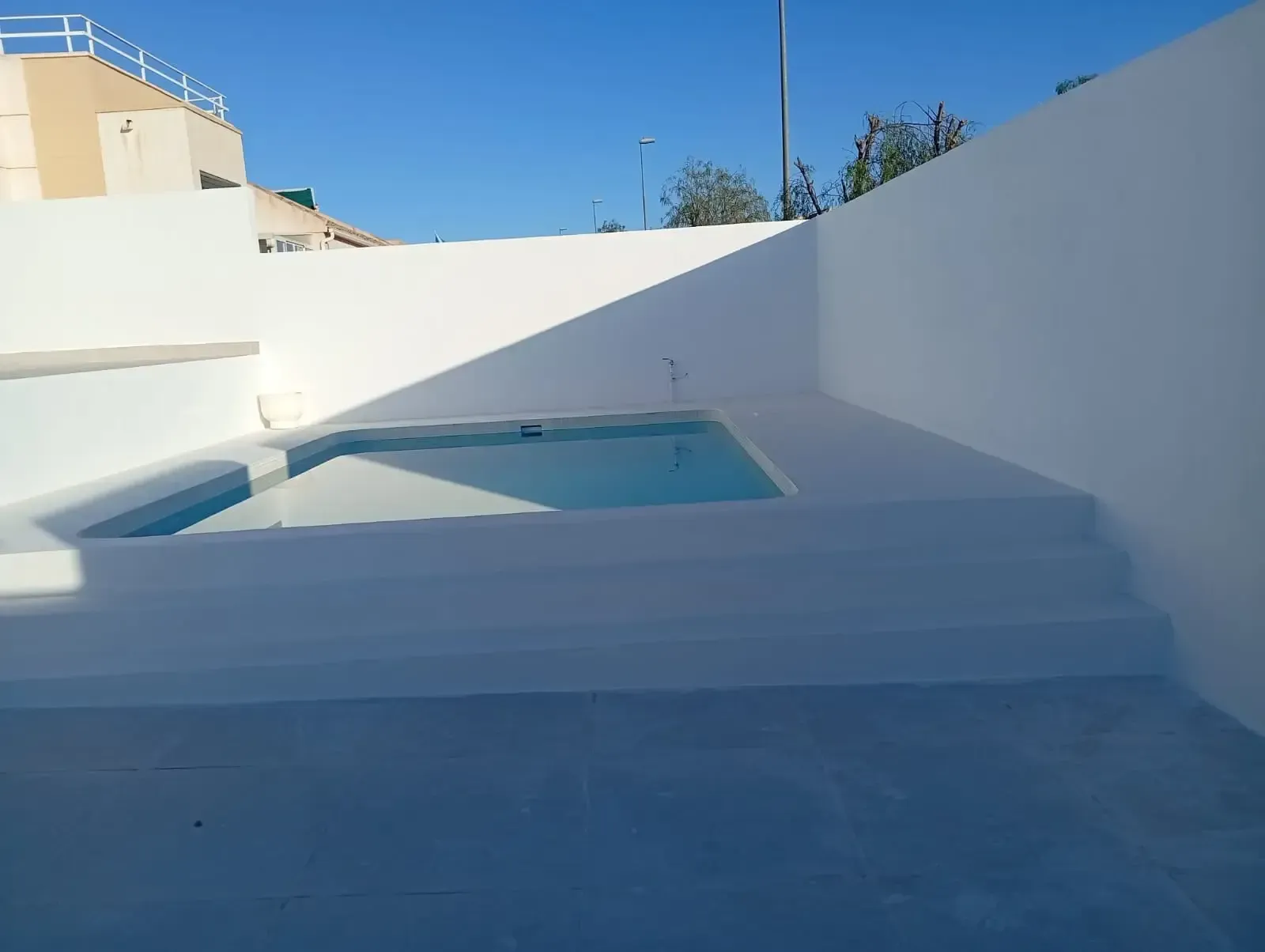 Patio de paredes blancas con una pequeña piscina azul bajo un cielo despejado.