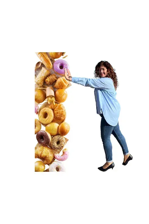 Mujer apartando con la mano una pared de diversos productos horneados, sonriendo. Lleva una camisa azul claro y vaqueros, sobre un fondo blanco.