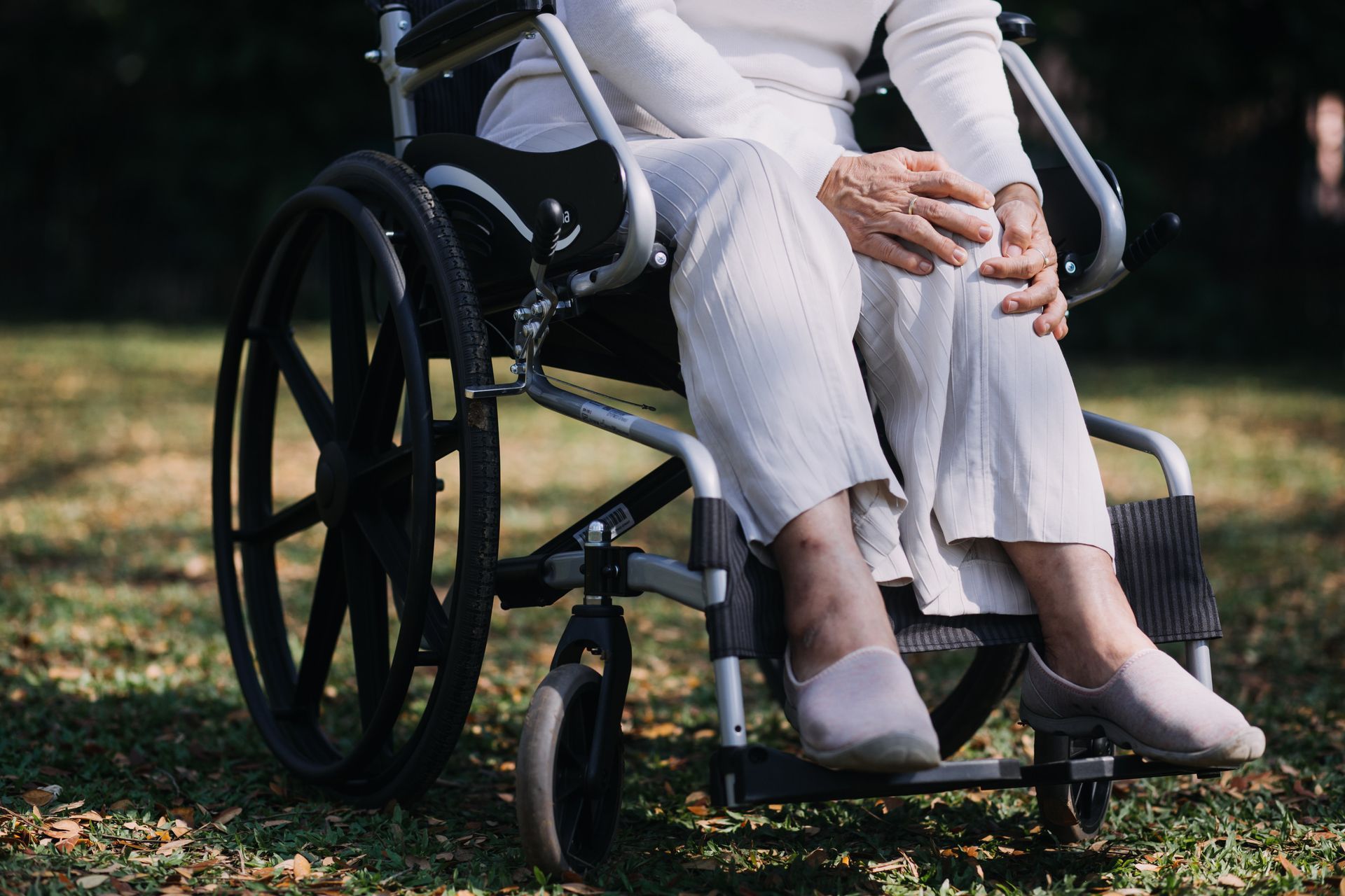Persona sentada en silla de ruedas al aire libre, sujetándose la rodilla.
