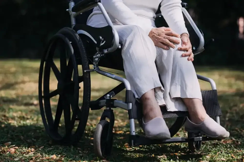 Persona sentada en silla de ruedas al aire libre, sujetándose la rodilla.