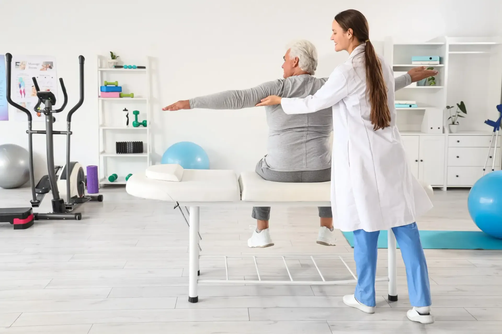 Fisioterapeuta ayudando a una persona con estiramientos de brazos en una clínica de rehabilitación.