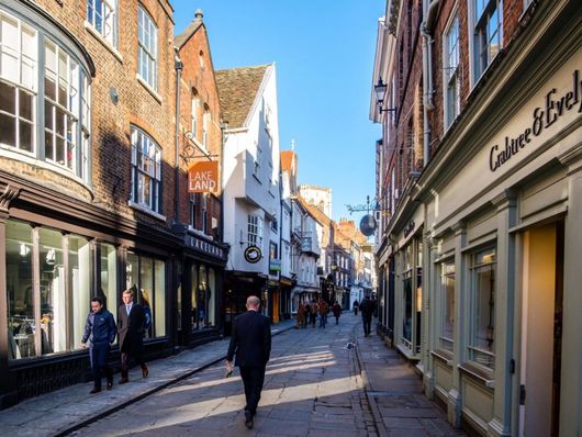 Narrow cobblestone street with shops and pedestrians in a sunny historic town center