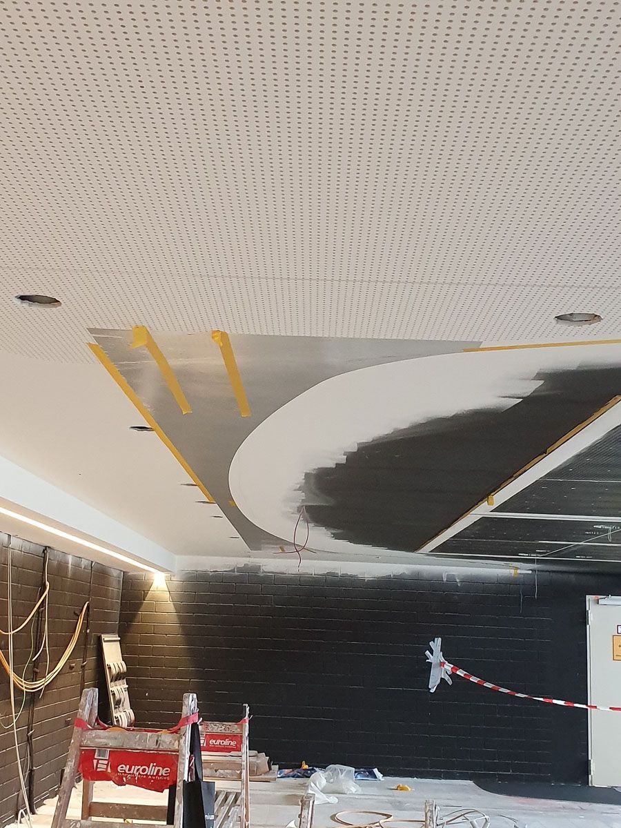 Eine Decke wird gestrichen und neben der Decke steht ein Schild - Referenzen der Malermeisterin Stefanie Würfel aus Bielefeld