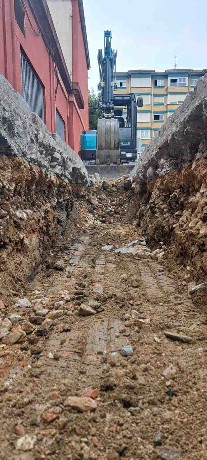 Estrecha zanja fangosa entre edificios, con laderas de tierra empinadas y un sendero de terreno húmedo e irregular.
