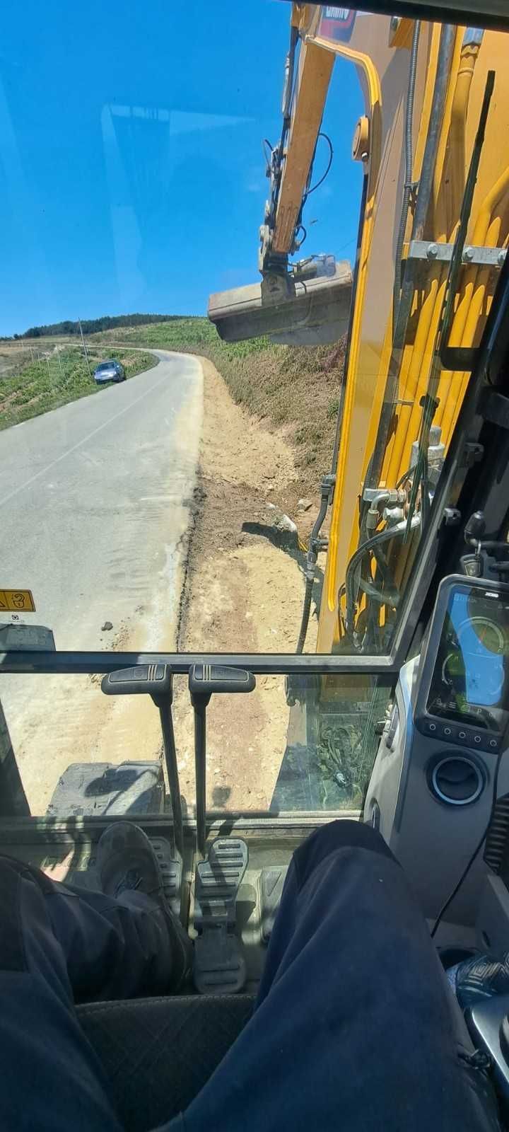 Dentro de la cabina de una excavadora amarilla que trabaja junto a una carretera en un día soleado.