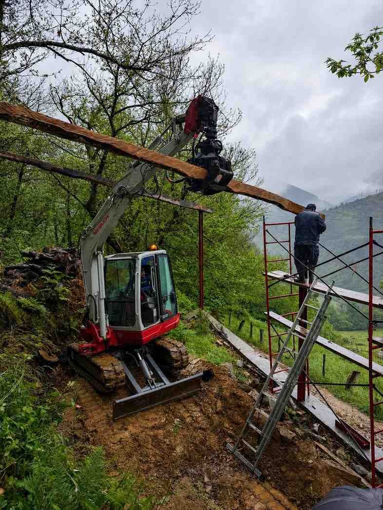 Trabajadores y una pequeña excavadora en una empinada ladera boscosa, instalando una línea debajo de un árbol caído.