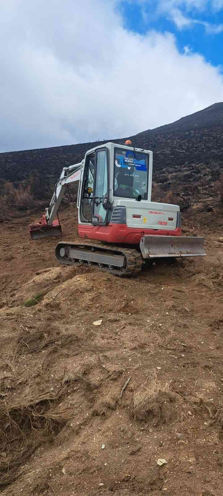 Excavadora blanca en una ladera fangosa bajo un cielo azul con nubes.